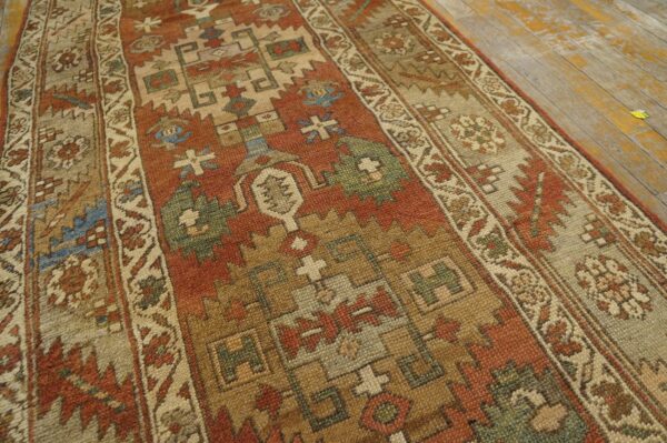 Close-up of a low-pile runner rug with geometric motifs in rust, tan, and blue on aged wooden floorboards.