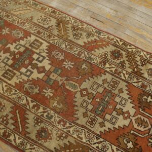 Rust and tan geometric runner rug displayed over distressed, light-colored wood plank flooring.