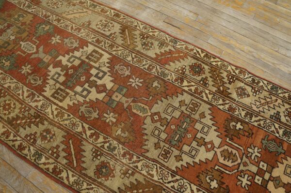 Rust and tan geometric runner rug displayed over distressed, light-colored wood plank flooring.