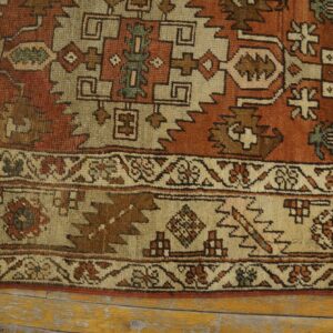 Close-up of a rustic rug with geometric patterns in rust, beige, brown, and hints of teal.