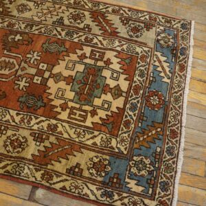 Rust, beige, and blue geometric rug with low pile on distressed, golden wood plank flooring.
