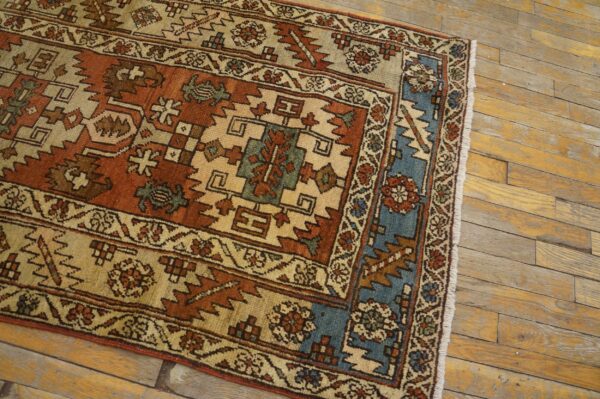 Rust, beige, and blue geometric rug with low pile on distressed, golden wood plank flooring.