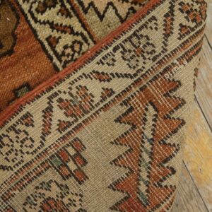 A close-up of a folded, burnt orange and beige geometric rug resting on rustic wood planks.