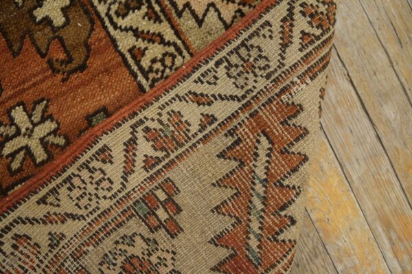 A close-up of a folded, burnt orange and beige geometric rug resting on rustic wood planks.