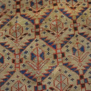 Close-up detail of a rug showing tan, red, and blue geometric patterns with tightly woven texture.
