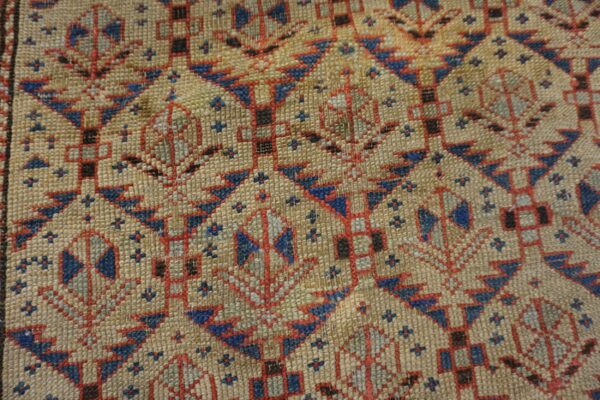 Close-up detail of a rug showing tan, red, and blue geometric patterns with tightly woven texture.