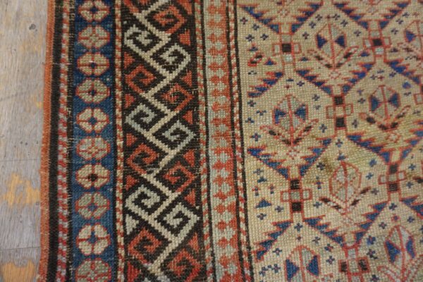 Geometric rug detail with borders in blue, red, and black on a tan field, resting on light wood.