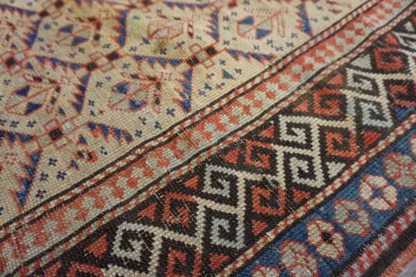 Low pile rug close-up showing beige field and bold borders with blue, red, and black geometric motifs.
