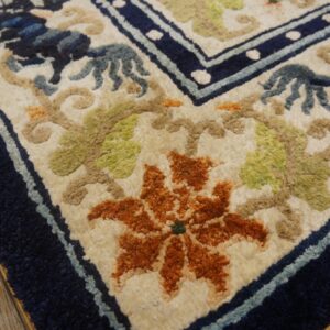 High-pile rug corner showing textured orange, green, and blue floral motifs with a navy border on wood flooring.