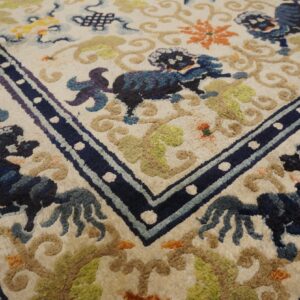Ivory rug detail showing blue guardian lion motifs, multicolored vines, and a navy blue border with white dots.