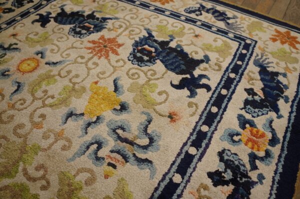 Textured pile rug with deep blue, orange, and green stylized patterns on a light field, bordered by navy trim.