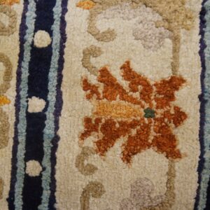 Close-up of textured orange floral and navy-striped rug on a cream field, bordering distressed wood planks.