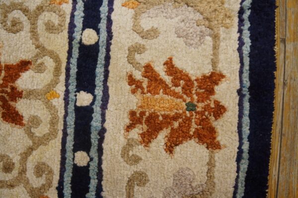 Close-up of textured orange floral and navy-striped rug on a cream field, bordering distressed wood planks.