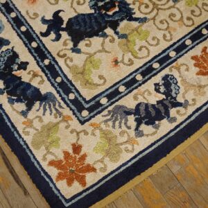 Textured cream rug featuring dark blue animal figures and orange flowers on worn yellow-toned wood flooring.