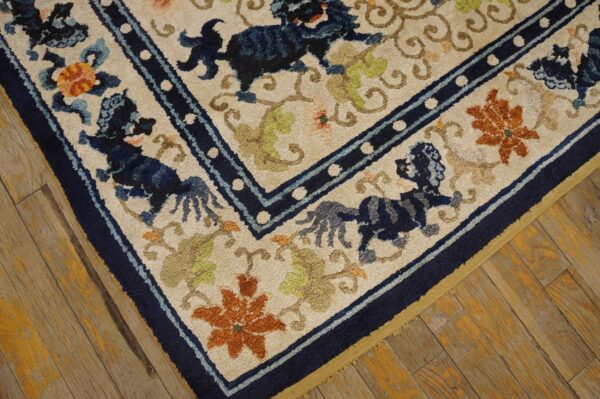 Textured cream rug featuring dark blue animal figures and orange flowers on worn yellow-toned wood flooring.