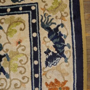 Textured cream rug with floral patterns in navy, orange, and green, bordered in dark blue on wood flooring.