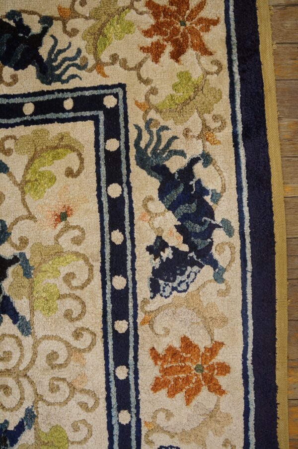 Textured cream rug with floral patterns in navy, orange, and green, bordered in dark blue on wood flooring.