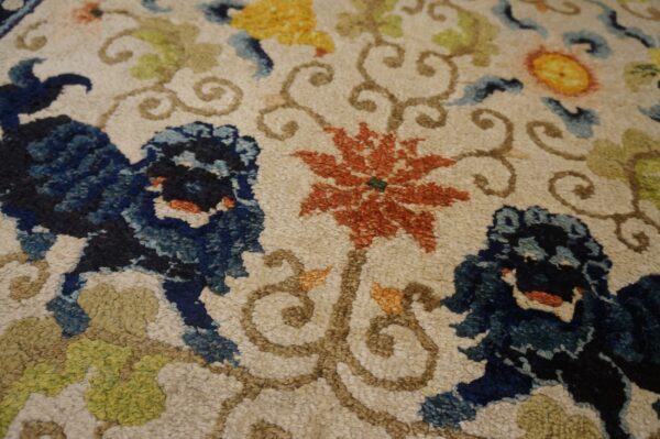 Textured rug detail with blue lion figures, rust flowers, and green scrolling vines on a cream background.