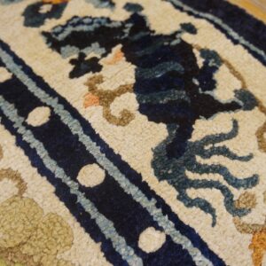 High-pile cream rug with navy, blue, and brown ornamental patterns lying on light wood flooring.