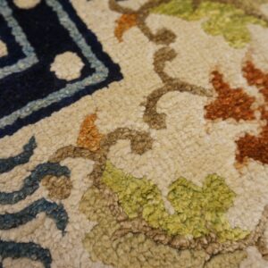 Close-up of a textured rug showing navy border and ivory field with green and rust floral pattern.