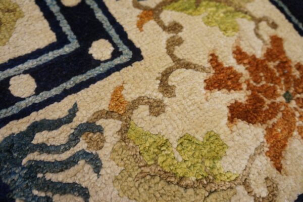 Close-up of a textured rug showing navy border and ivory field with green and rust floral pattern.