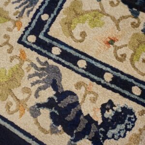 Textured rug featuring a navy blue border, orange florals, and a stylized blue creature on a light cream background.