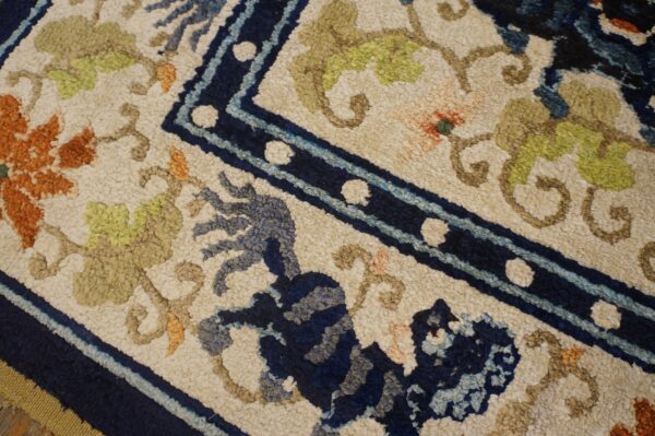 Textured rug featuring a navy blue border, orange florals, and a stylized blue creature on a light cream background.