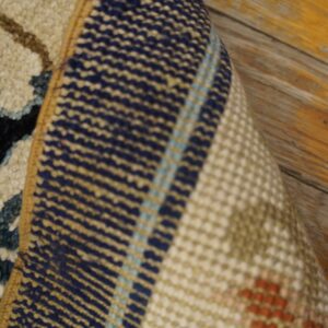 Close-up of a rug corner folded, showing textured navy and cream pile against a multicolored woven backing.