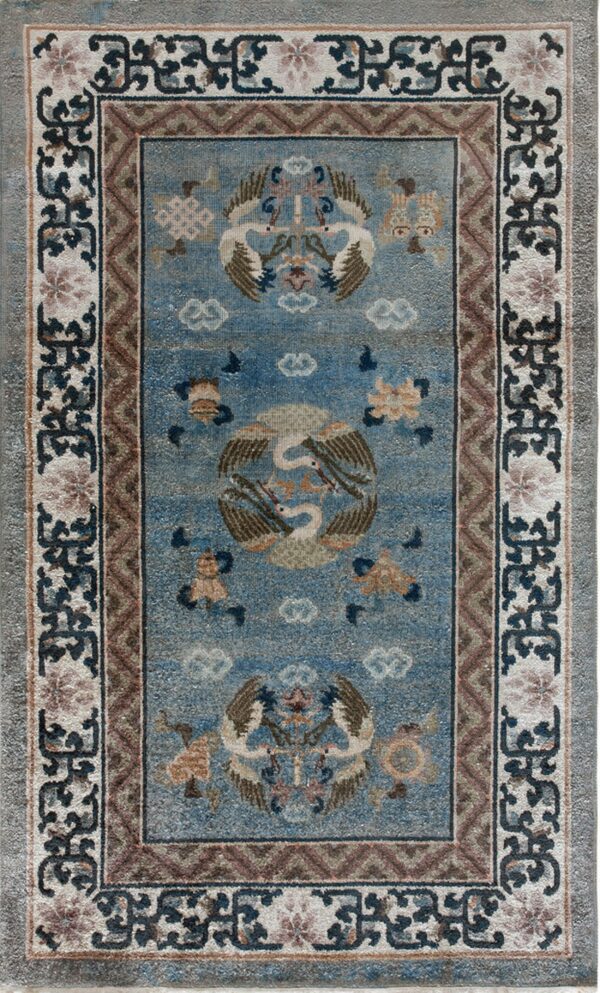 Muted blue rug with brown and cream borders, centered with traditional stylized cranes and cloud motifs.