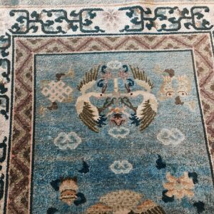 Close-up of a distressed blue rug featuring central cranes, floral patterns, and intricate multi-colored borders.