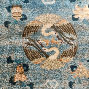 Low-pile, muted blue rug with a central design of two beige birds and a patterned border.
