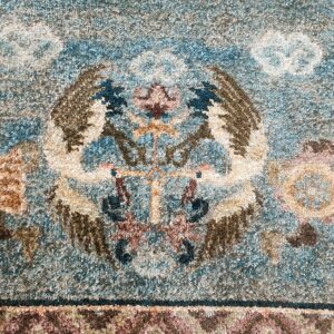Textured high pile rug detail with a symmetrical winged blue, brown, and cream central motif.