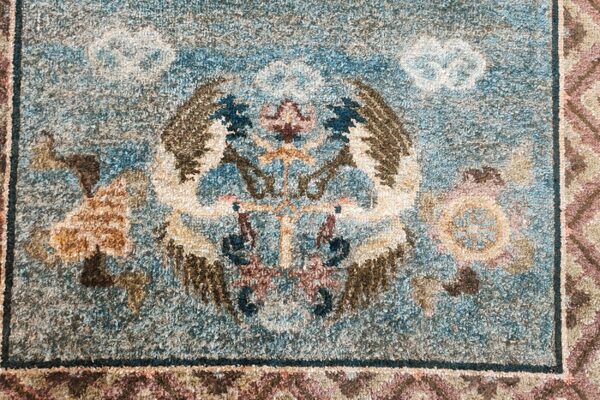 Textured high pile rug detail with a symmetrical winged blue, brown, and cream central motif.