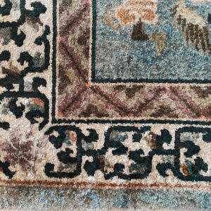Plush, high-pile rug detail showing teal, beige, and dark brown traditional borders and scrollwork.