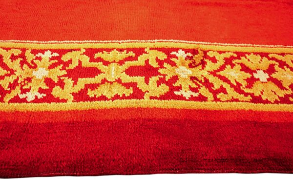 Detail of a vibrant red rug featuring a gold, yellow, and white decorative patterned band.