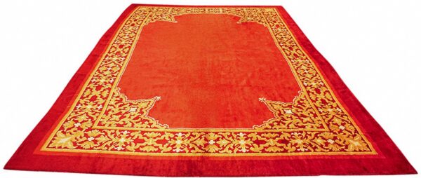 Large, low-pile red rug featuring a central field bordered by an intricate gold floral design.