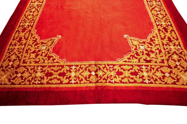 High-pile orange-red rug featuring elaborate gold foliate motifs along the patterned perimeter border.