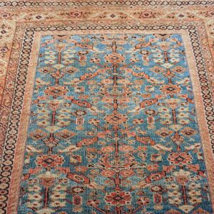 Low-pile patterned rug with a blue field and coral botanical motifs, framed by multi-striped peach borders.