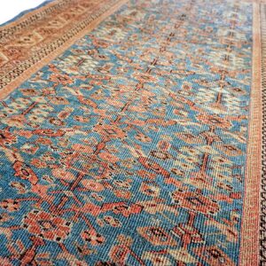 Traditional rug featuring a blue patterned field bordered by wide bands of rust, tan, and cream motifs.