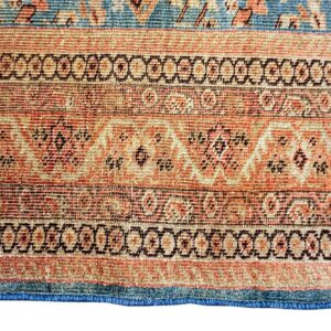 Close-up of a low pile rug featuring alternating bands of rust, peach, teal, and brown traditional patterns.