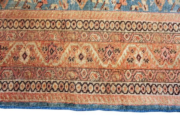 Close-up of a low pile rug featuring alternating bands of rust, peach, teal, and brown traditional patterns.
