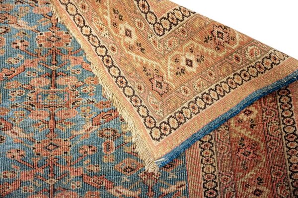 Close-up of a low-pile rug folded, showing the contrasting blue field and tan/coral patterned border.