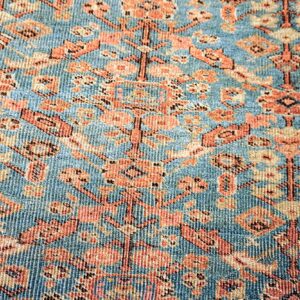 Blue rug detail showing dense orange, peach, and beige stylized floral motifs with a ribbed texture.