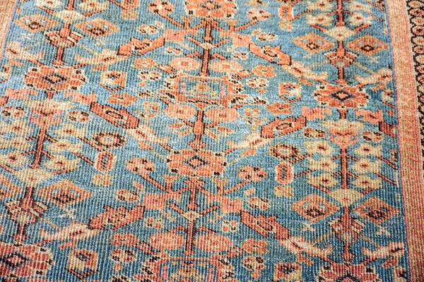 Blue rug detail showing dense orange, peach, and beige stylized floral motifs with a ribbed texture.
