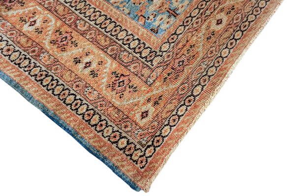 Detailed view of a rug corner featuring orange, tan, and blue colors with multiple geometric and floral borders.