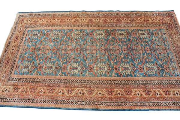 A rectangular rug featuring a dense traditional pattern in teal blue, rust, and beige colors.
