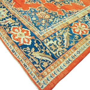 Detailed corner of an ornate rug in rust orange, blue, and cream with complex floral and animal borders.