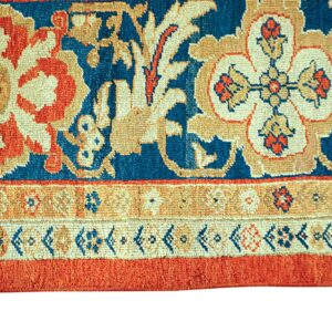 High-pile blue rug with tan and orange floral designs transitions to a structured multi-striped border.