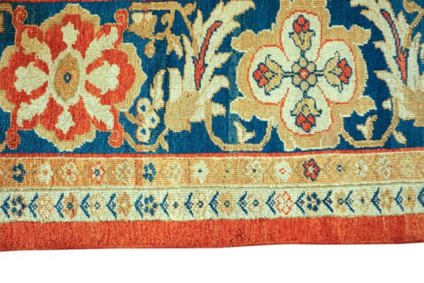 High-pile blue rug with tan and orange floral designs transitions to a structured multi-striped border.