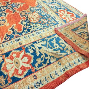 A rust red and navy patterned rug corner is folded over, showing the ornate main field and detailed border.